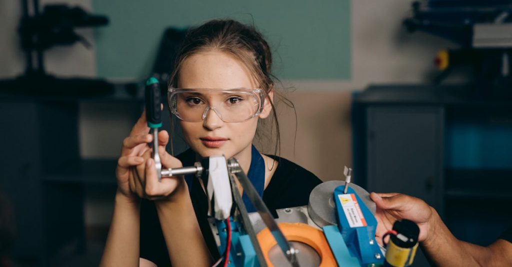 A young woman with goggles uses a tool in a workshop environment, focusing intently on her task.